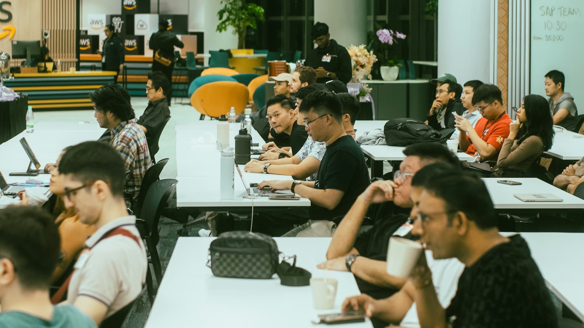 Rows of hackathon tables with teams building on laptops